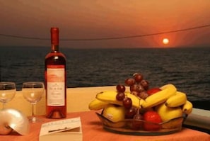 A table with a bottle of wine, glasses, and a fruit bowl with bananas and grapes.