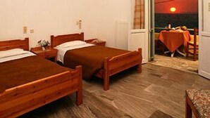 A bedroom with two wooden beds, a small table with a chair, and a view of the sunset through an open door. - Nautilus Apartments (Agios Nikolaos)