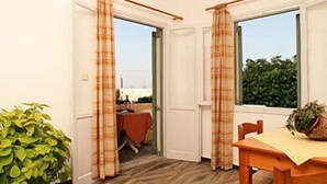 A room with a wooden floor, a dining table with chairs, a potted plant, and a view through a window. - Nautilus Apartments (Agios Nikolaos)