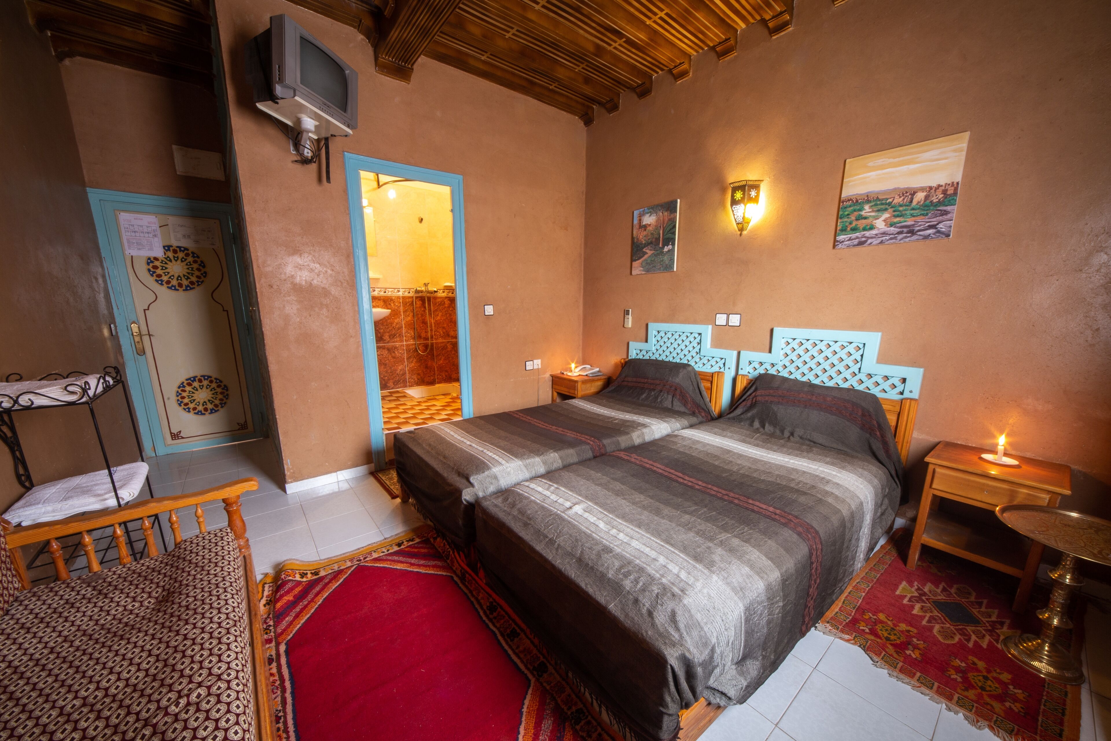 A bedroom with two beds, a TV, a nightstand with a lamp, and a red carpet.