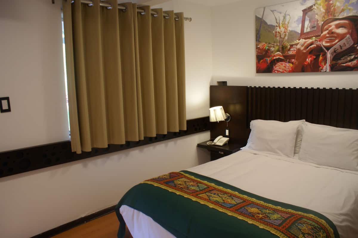 A hotel room with a bed, a nightstand with a lamp, a telephone, and a painting on the wall.