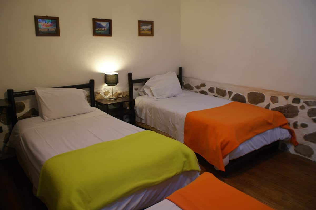 A room with two beds, each with a different colored blanket, a nightstand with a lamp, and three framed pictures on the wall.