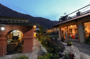 Un edificio con un arco de ladrillo en la entrada, un camino de piedra y un jardín con diversas plantas.