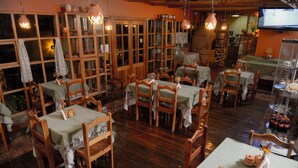 Un restaurante con mobiliario de madera, mesas con manteles, luces colgantes y un televisor en la pared.