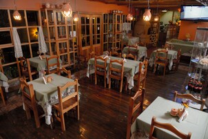 Un restaurante con mobiliario de madera, mesas con manteles, luces colgantes y un televisor en la pared.