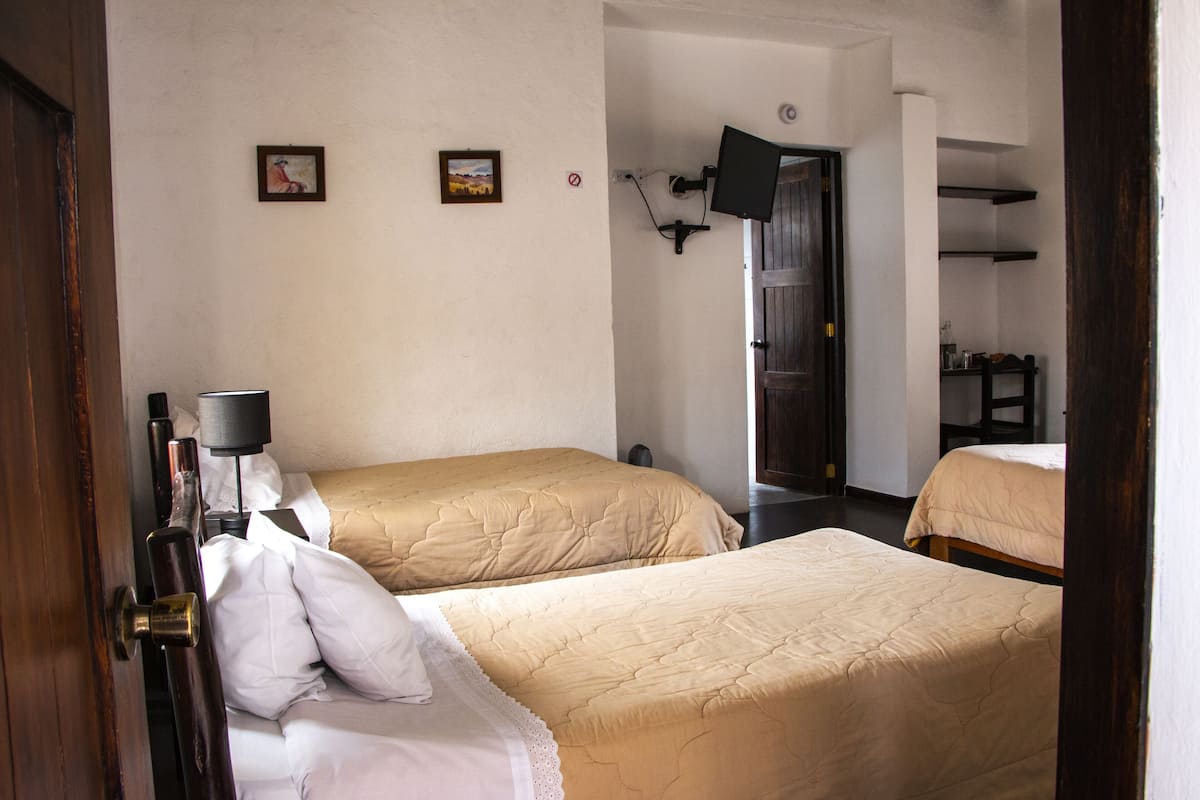 A hotel room with two beds, a flat-screen TV mounted on the wall, and a door leading to another room.