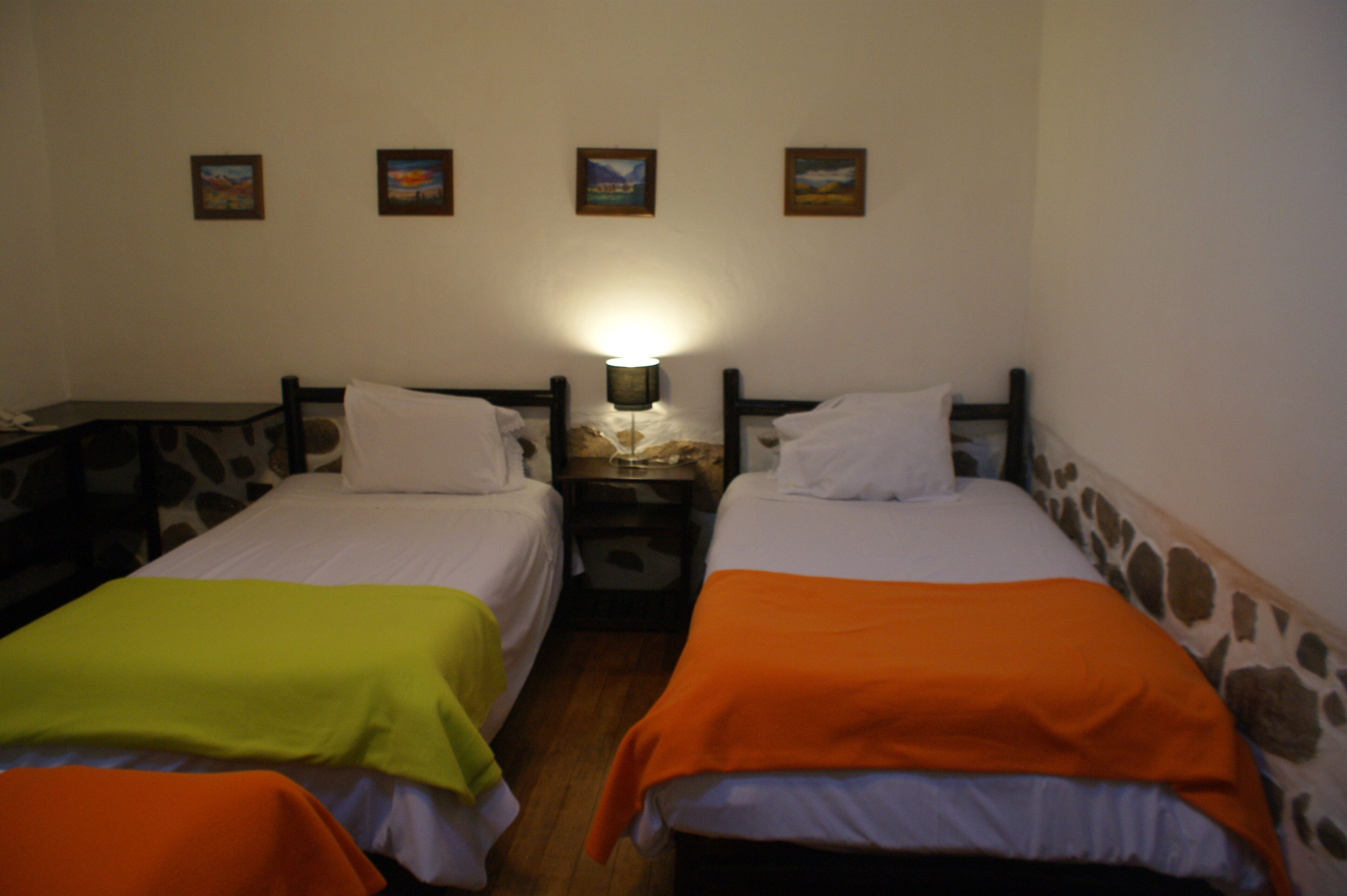 A room with two beds, a nightstand, and a wall-mounted lamp.