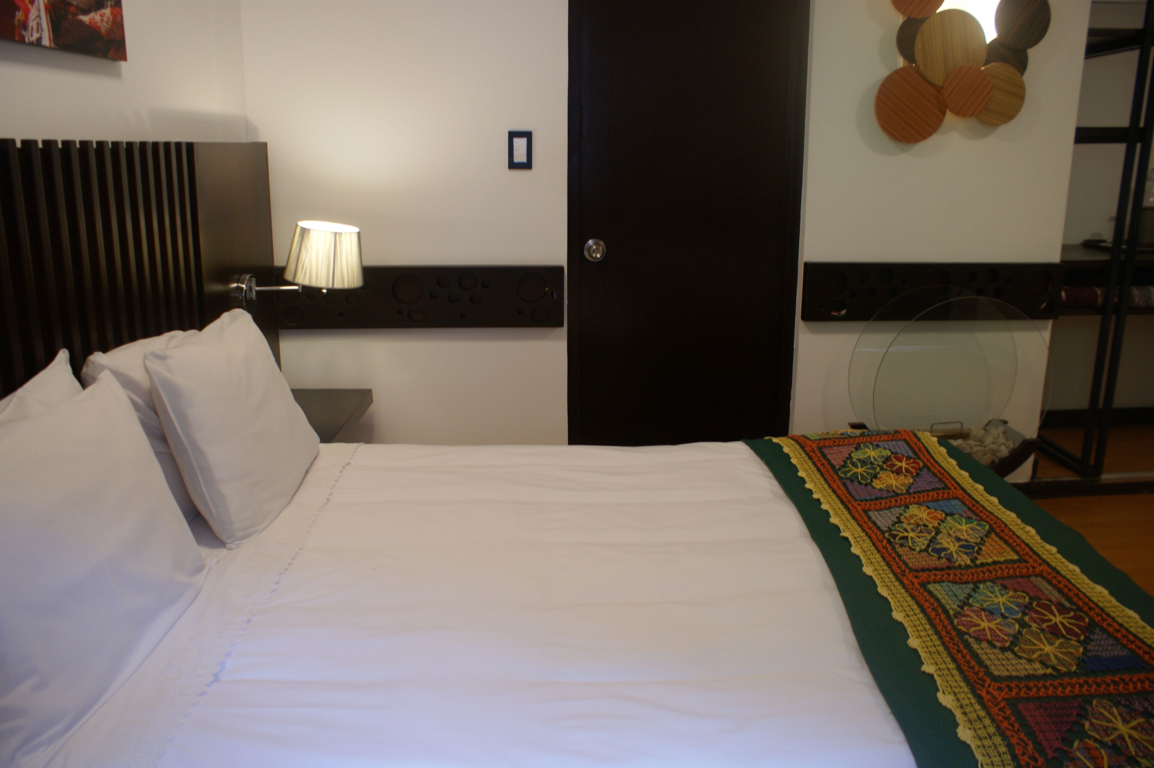 Una habitación de hotel con cama, mesita de noche, lámpara, puerta y un adorno en la pared.