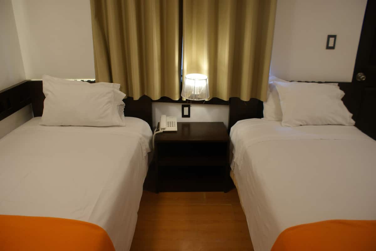 A hotel room with two beds, a nightstand with a phone, and a window with curtains.