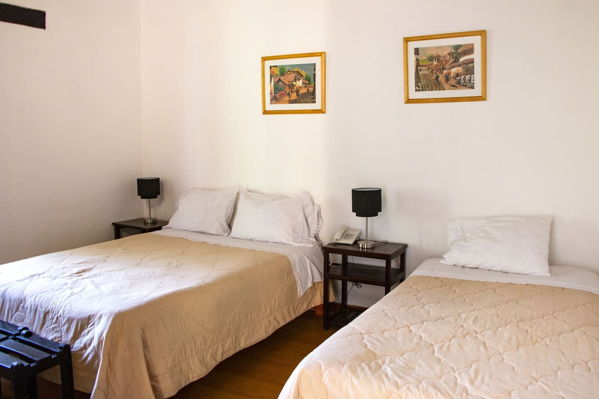 A hotel room with two single beds, a bedside table with a lamp, and two framed pictures on the wall.