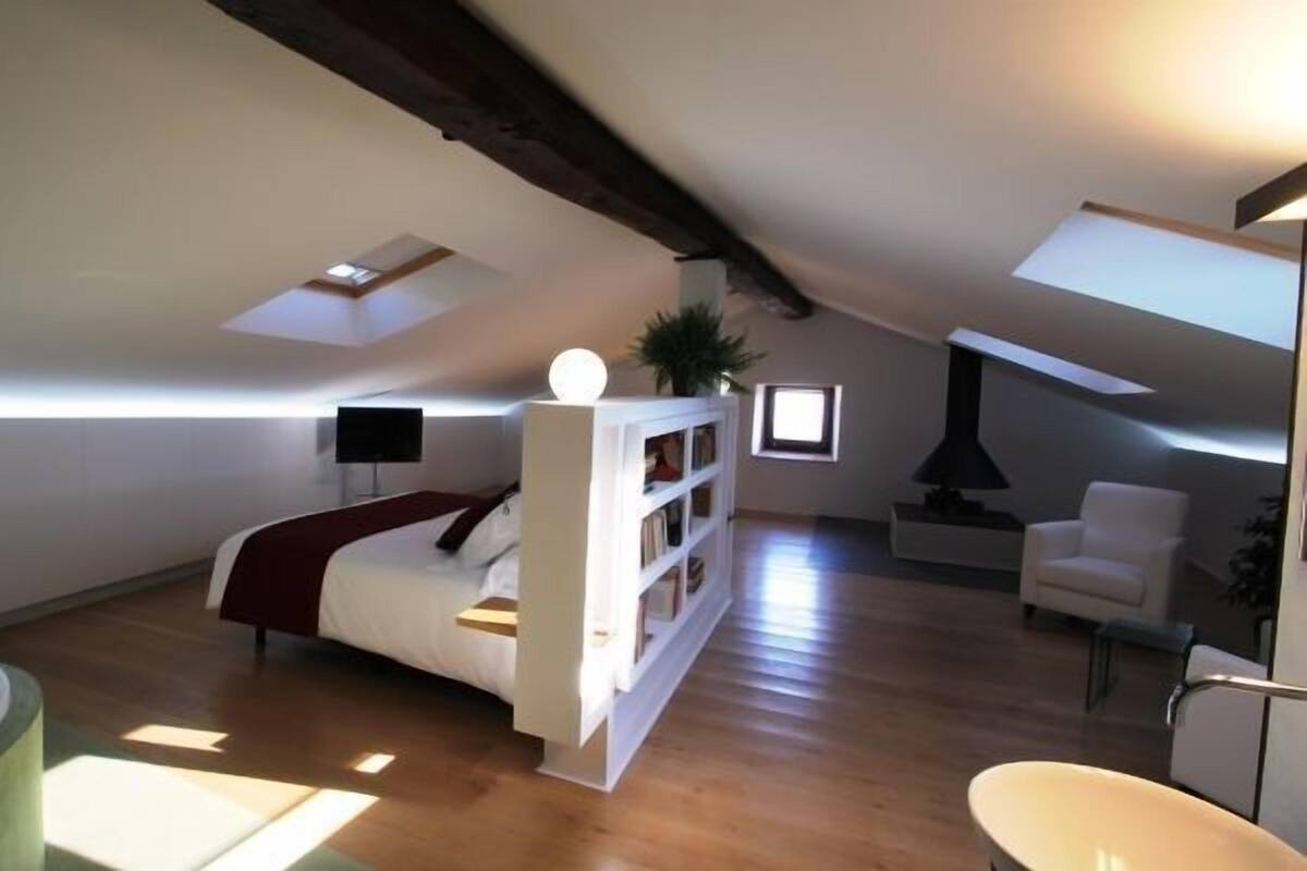 Quarto estilo loft com cama, estantes embutidas, televisão e lareira.