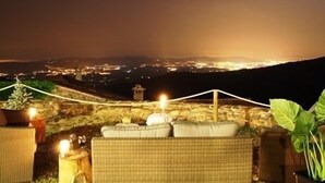 Un espacio al aire libre con mobiliario de mimbre, un muro de piedra y vistas a una ciudad de noche.