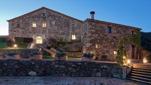 Un edificio de piedra con techo de tejas, una escalera que conduce a la entrada y un muro de piedra en primer plano.