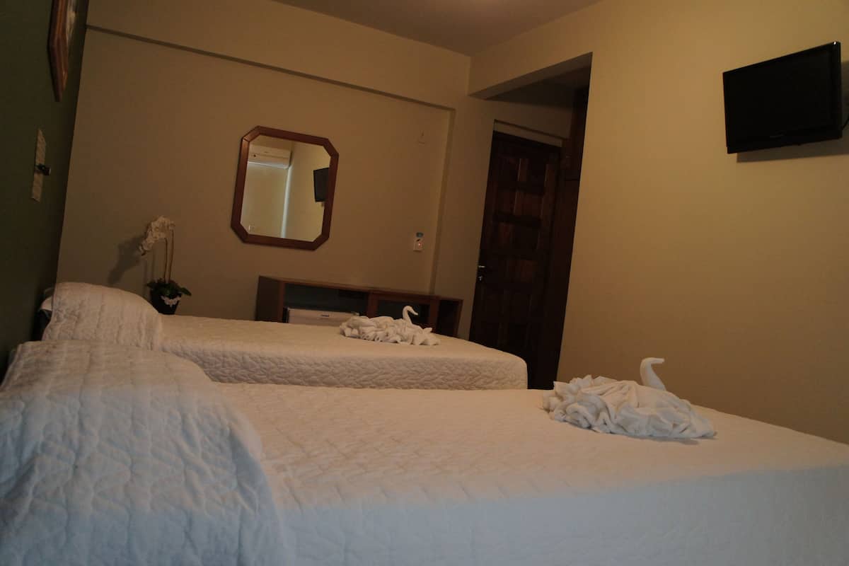 A hotel room with two beds, a mirror, and a television on the wall.