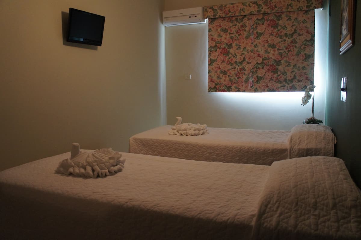 Two single beds with white bedding, a television on the wall, and a floral window blind.
