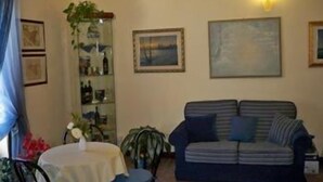 A living room with a sofa, a table with a white tablecloth, and a bookshelf with various items. - Marchese Sala (Agrigento)