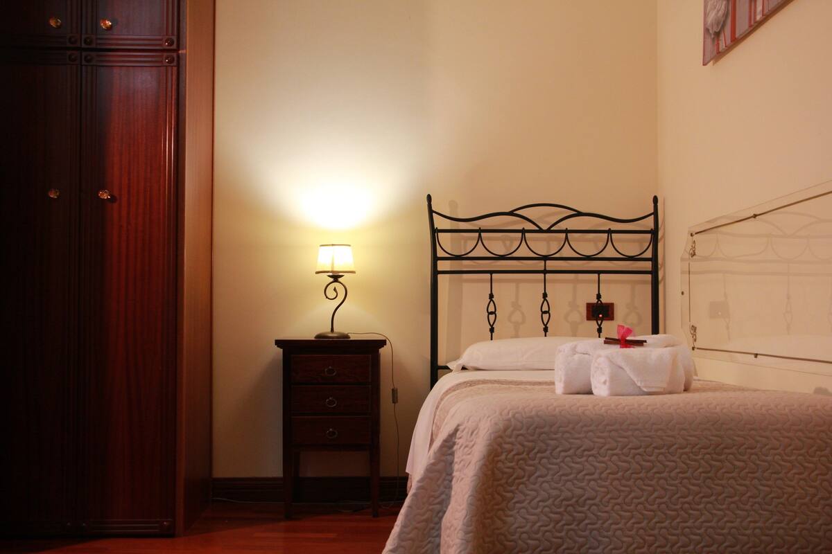 Un dormitorio con cama, mesita de noche, lámpara y armario.