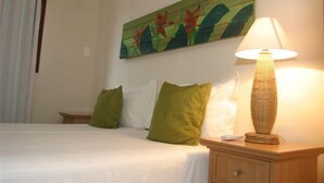 A neatly made bed with green pillows, a bedside table with a lamp, and a wall painting. - CostaSol Pipa (Tibau do Sul)