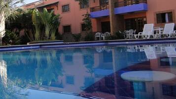 A swimming pool with a clear blue water surface, surrounded by white lounge chairs and a building with balconies.