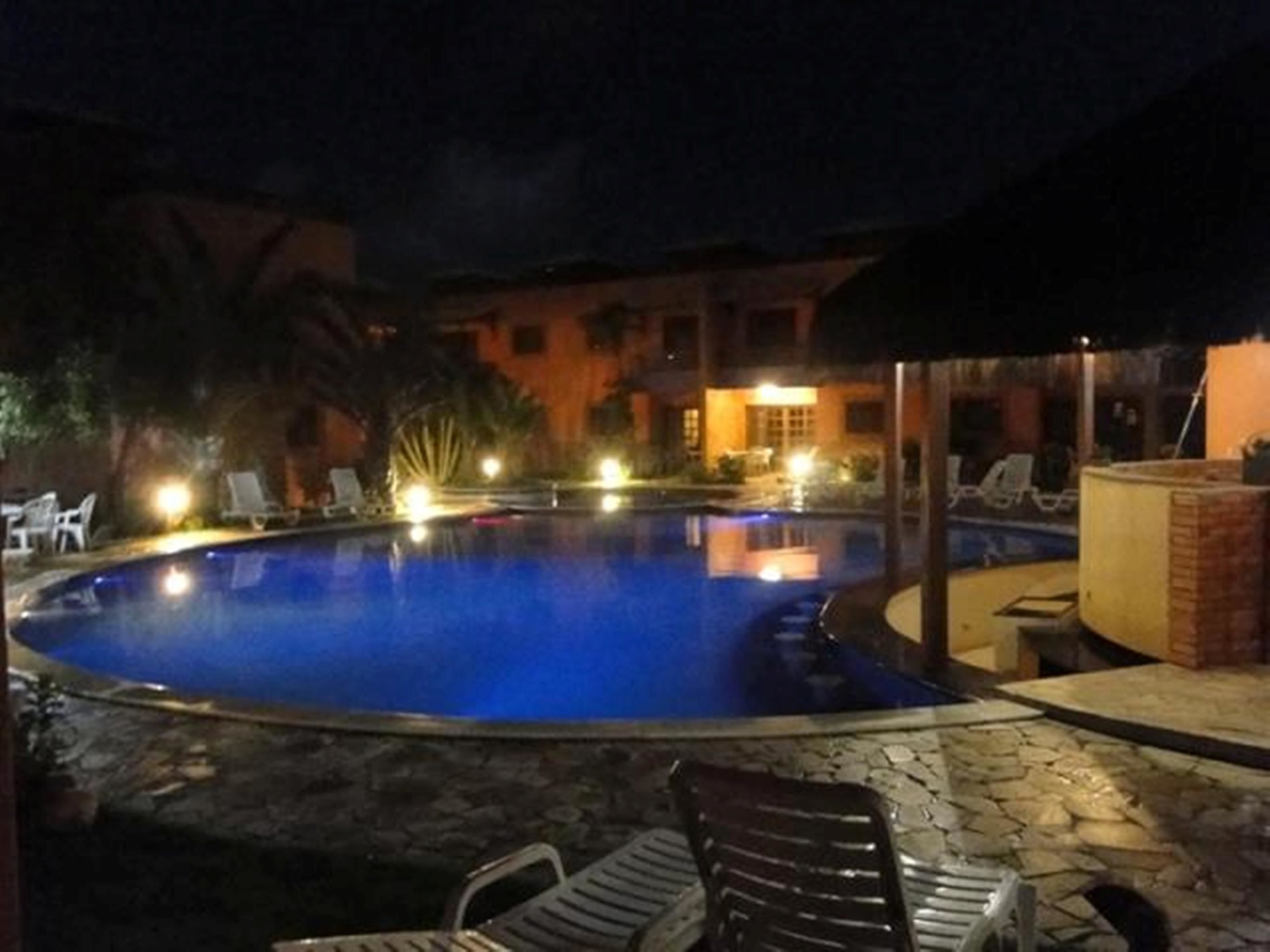 Vista nocturna de una piscina con sillones de descanso y un edificio al fondo.