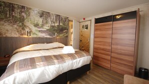 A bedroom with a large bed, a wardrobe, and a forest-themed wall mural. - Bij hen op Ameland (Hollum)