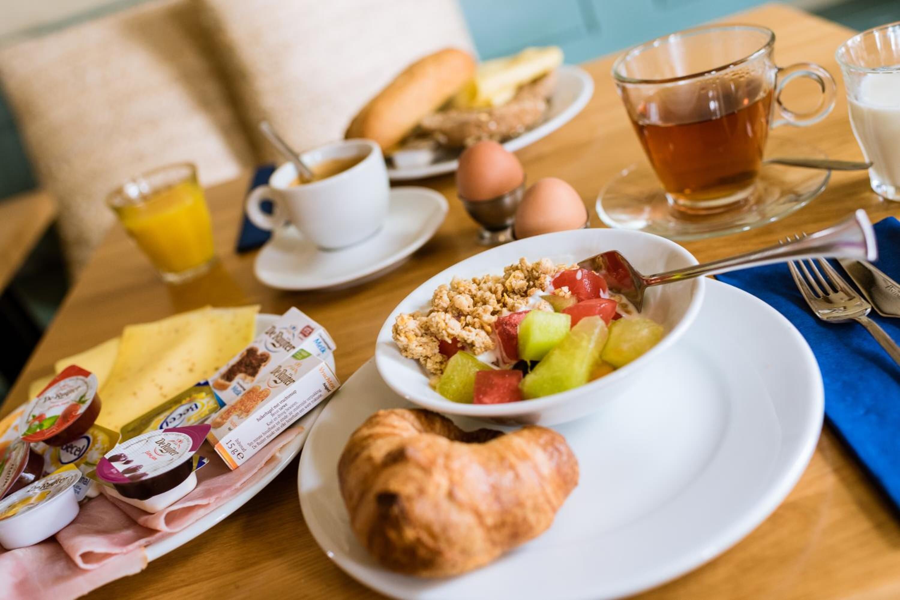 A breakfast table with croissants, a bowl of fruit, eggs, and a cup of tea.