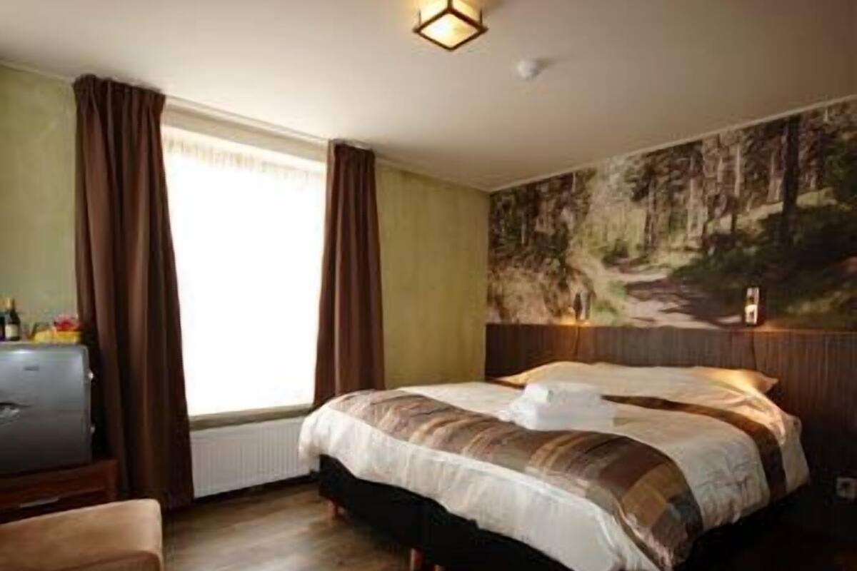 A bedroom with a bed, a dresser, a chair, a window with curtains, and a wall mural.