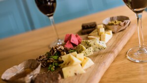 A wooden board with various cheeses, nuts, and a bowl of fruit. Two glasses of red wine are on the table. - Bij hen op Ameland (Hollum)