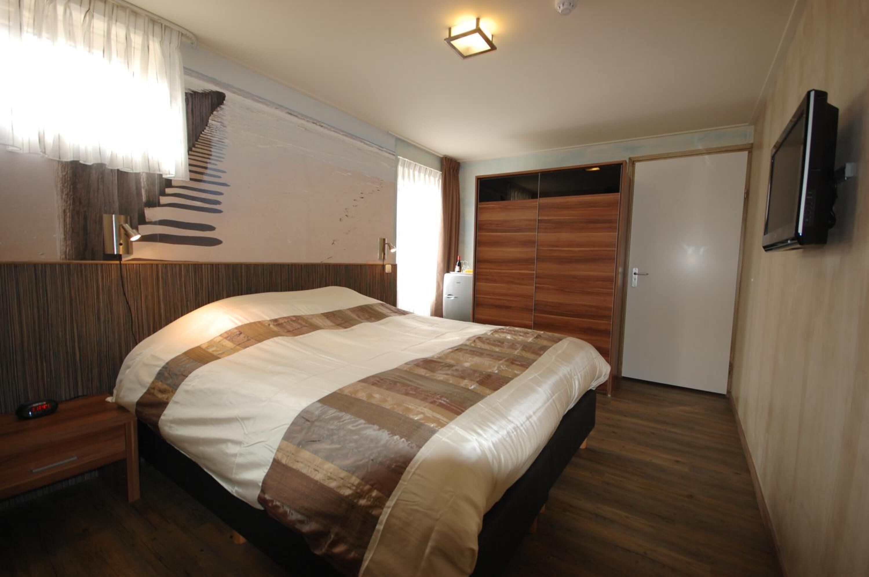 A bedroom with a large bed, wooden flooring, a TV mounted on the wall, and a wardrobe.
