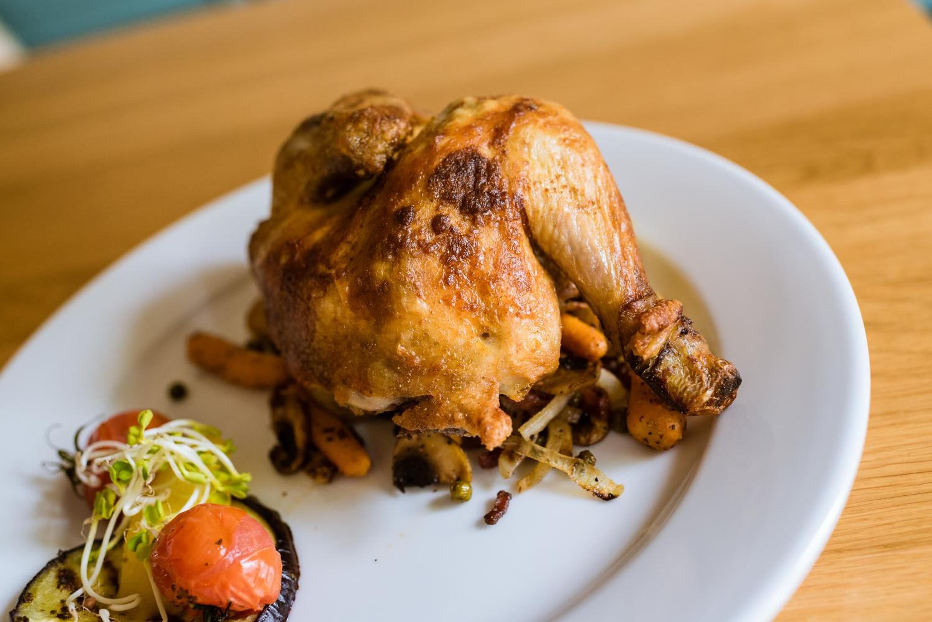 Pollo asado sobre un plato blanco, con verduras rostizadas y una ensalada pequeña.