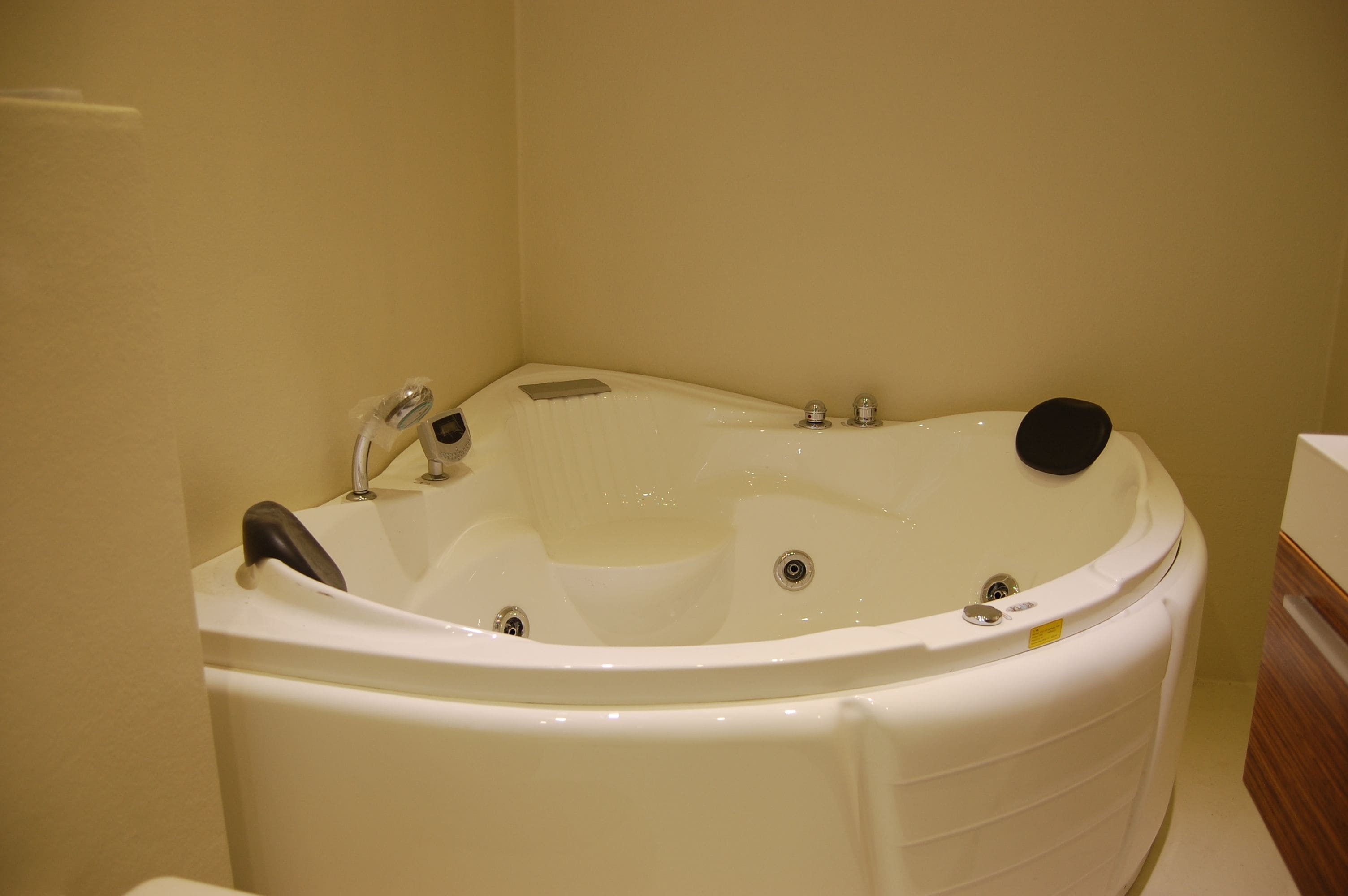 A white bathtub with a black seat, a handheld showerhead, and a control panel.