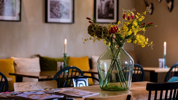 A dining area with a table set for two, featuring a vase with yellow flowers and candles. - Bij hen op Ameland (Hollum)