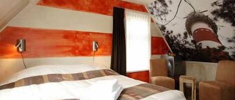 A hotel room with a bed, a small table, a chair, and a wall with a tree mural.