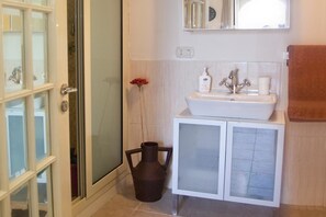 A bathroom with a glass shower enclosure, a white sink with a mirror above, and a brown vase on the floor. - B&B Garibaldi Catania (Catania)