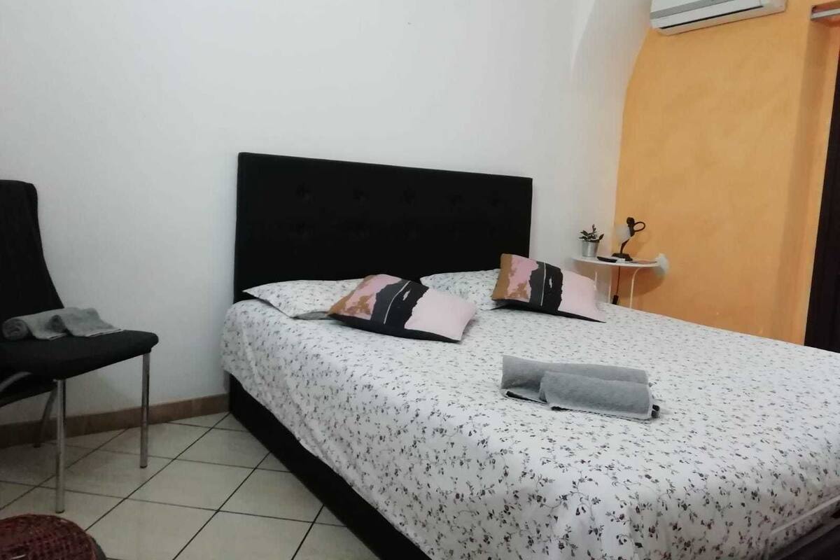 Ein Schlafzimmer mit Bett, Sessel, Nachttisch und Klimaanlage.