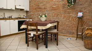 A kitchen with white cabinets, a brick wall, a dining table with chairs, and a small stand with a book. - B&B Garibaldi Catania (Catania)
