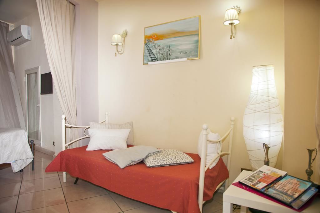 A bedroom with a single bed, a nightstand, a painting, and two wall-mounted lamps.