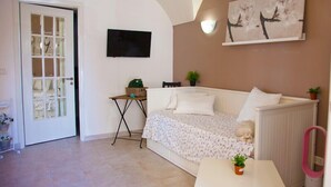 A living room with a white sofa, a small table, a TV mounted on the wall, and a door with a glass panel. - B&B Garibaldi Catania (Catania)