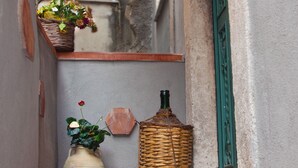 A narrow outdoor corridor with a tiled floor, a wicker basket, a ceramic vase with flowers, and a green door frame. - B&B Garibaldi Catania (Catania)
