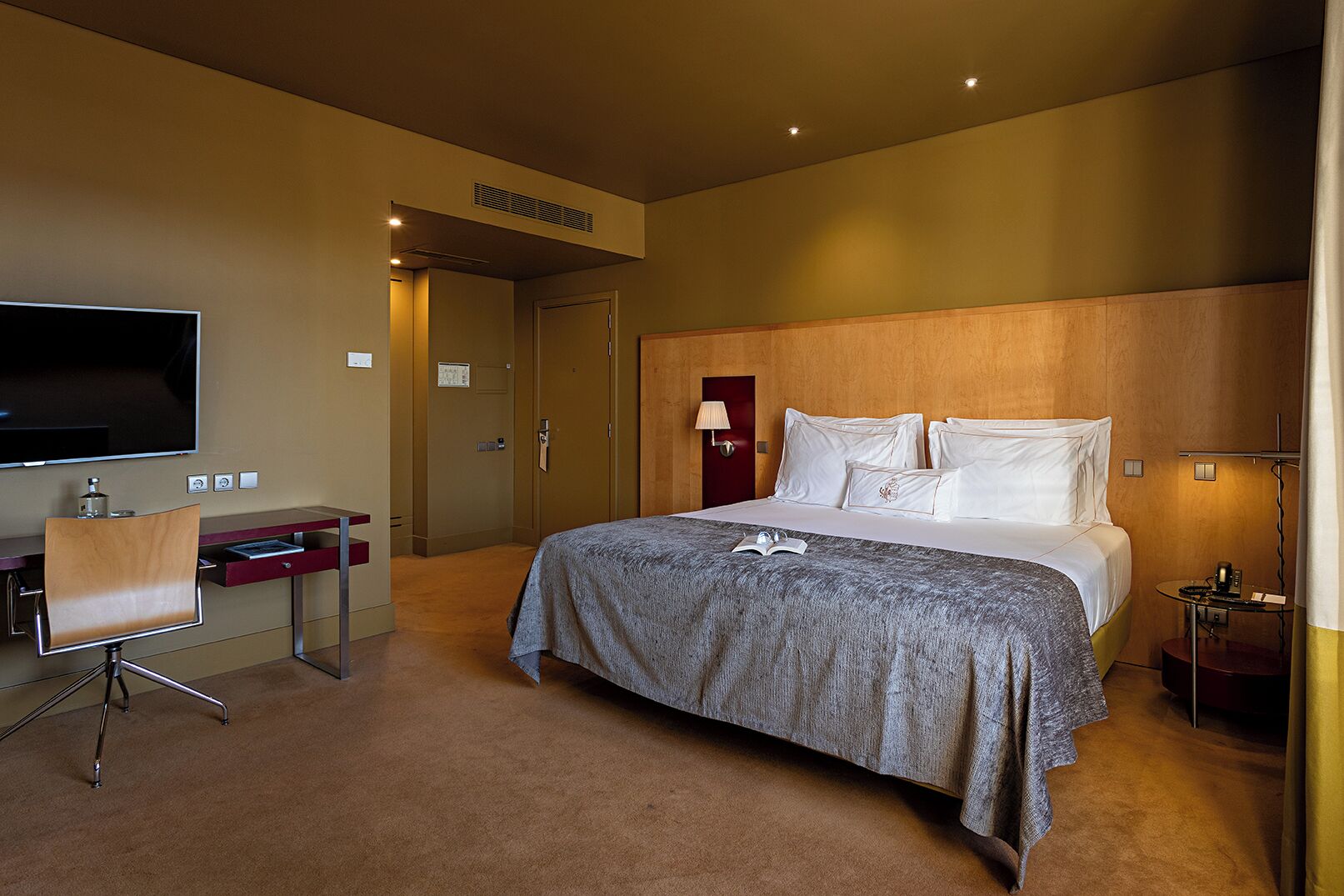 A hotel room with a bed, a desk, a TV, and a lamp.