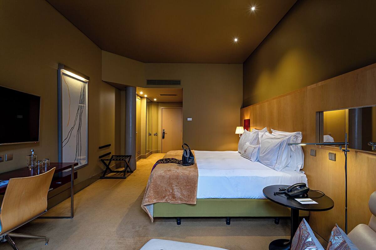Una habitación de hotel con cama, mesita de noche, silla, escritorio, televisión y obras de arte.