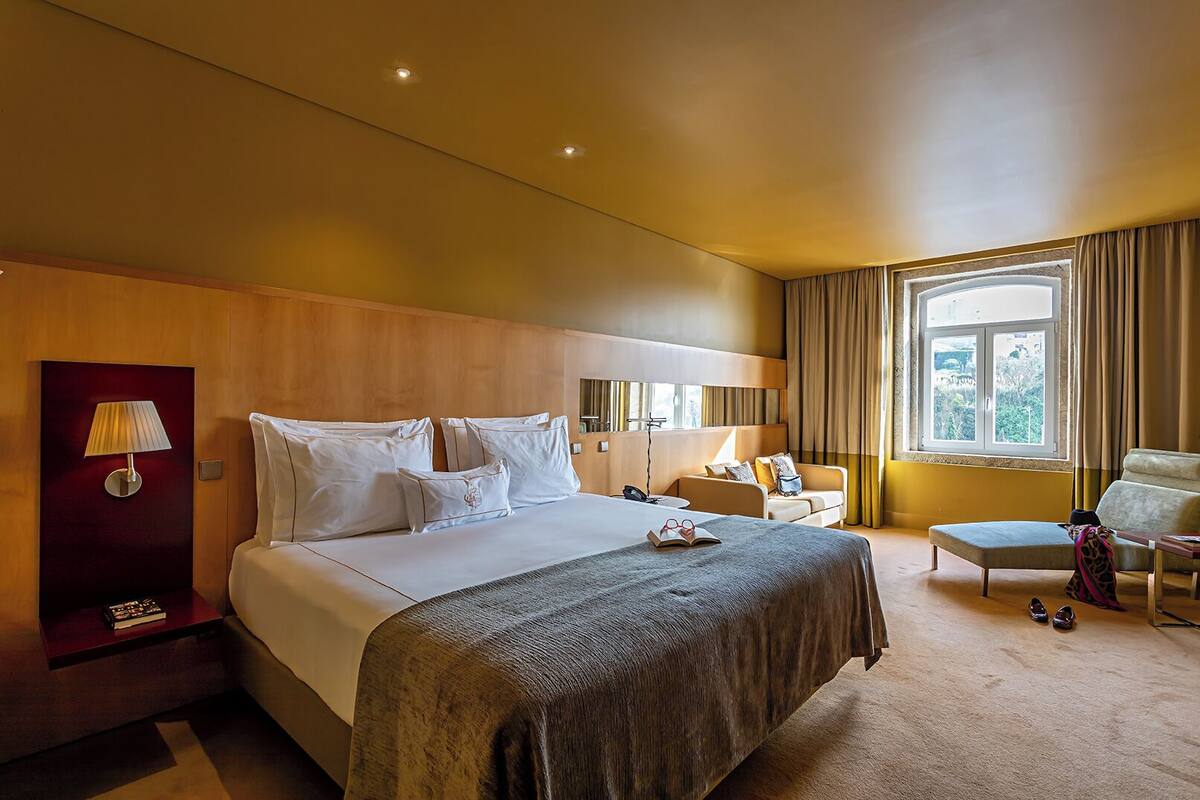 Habitación de hotel con una cama grande, mesitas de noche, un escritorio, una silla y una ventana con cortinas.