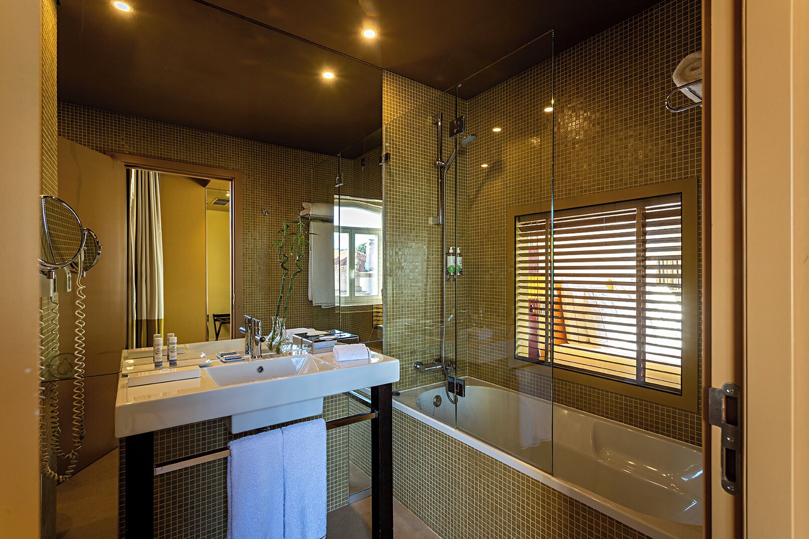 A modern bathroom with a large mirror, two sinks, a bathtub, and a shower area.