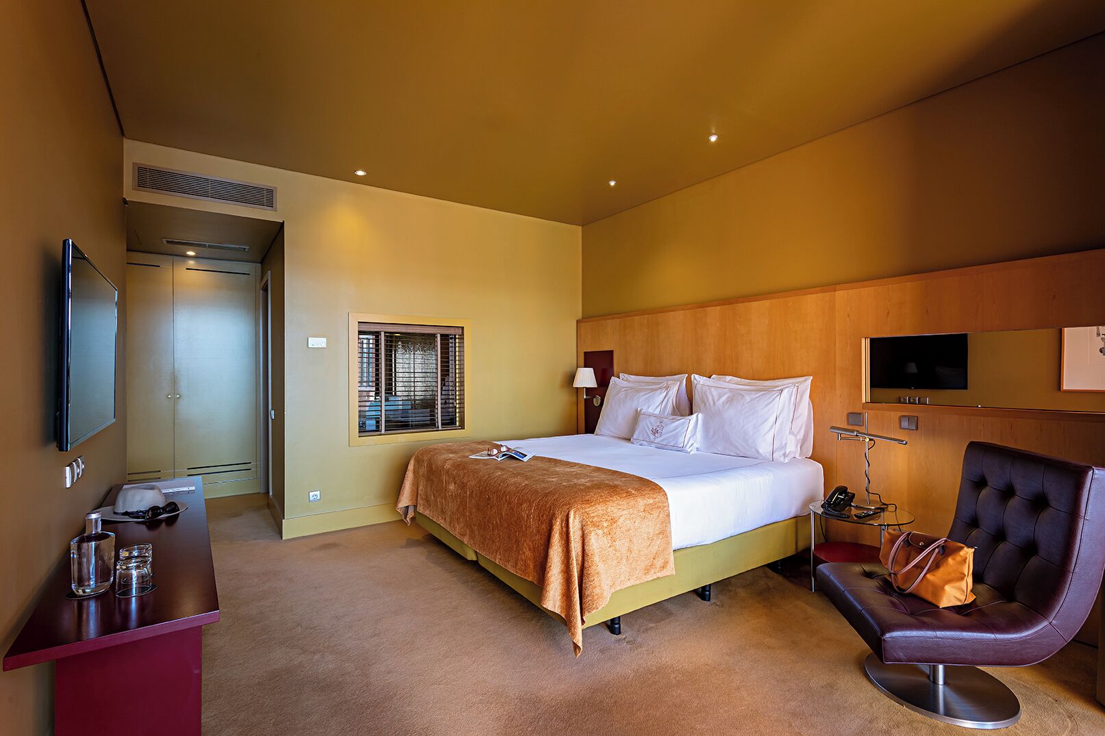 A hotel room with a bed, a desk with a chair, a TV, and a window with blinds.