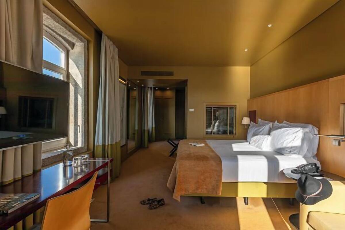 Habitación de hotel con cama, escritorio, silla y vistas por la ventana.