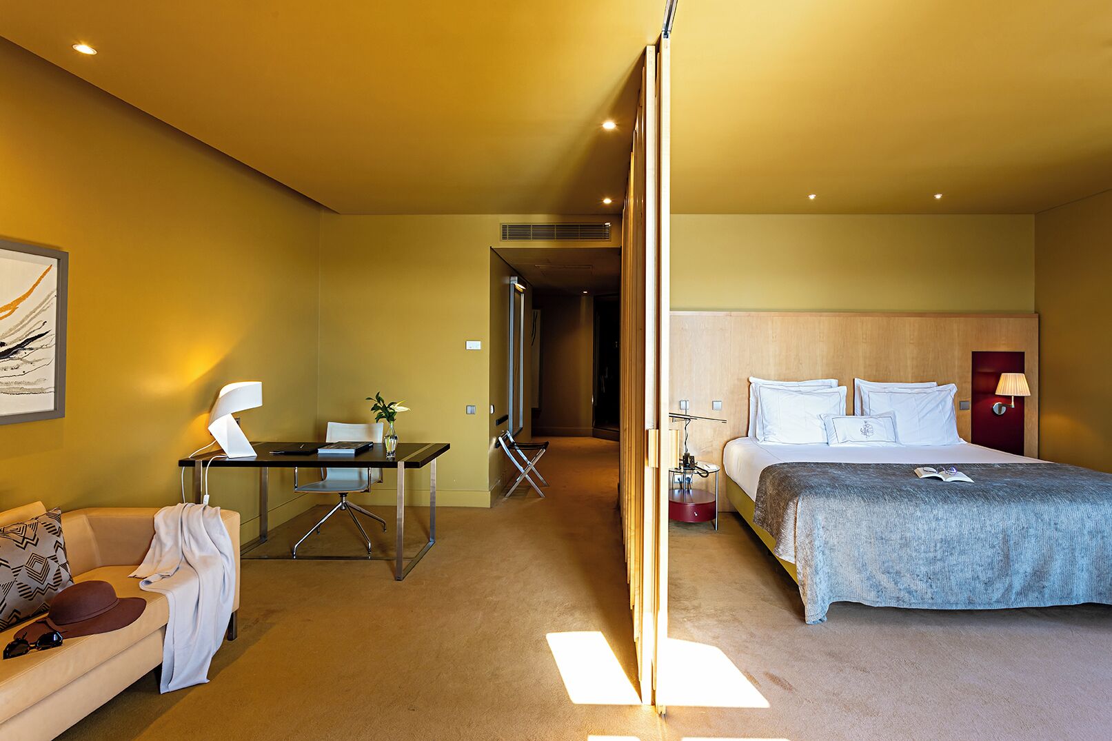 Una habitación de hotel con cama, escritorio, silla, sofá y televisor montado en la pared.