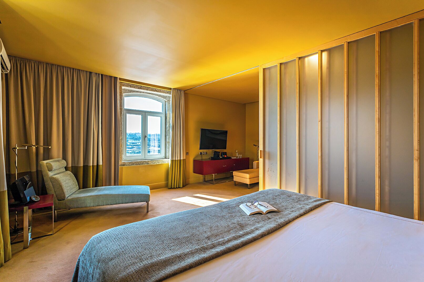Une chambre d’hôtel avec un lit, un bureau, une chaise, une télévision et une fenêtre avec des rideaux.