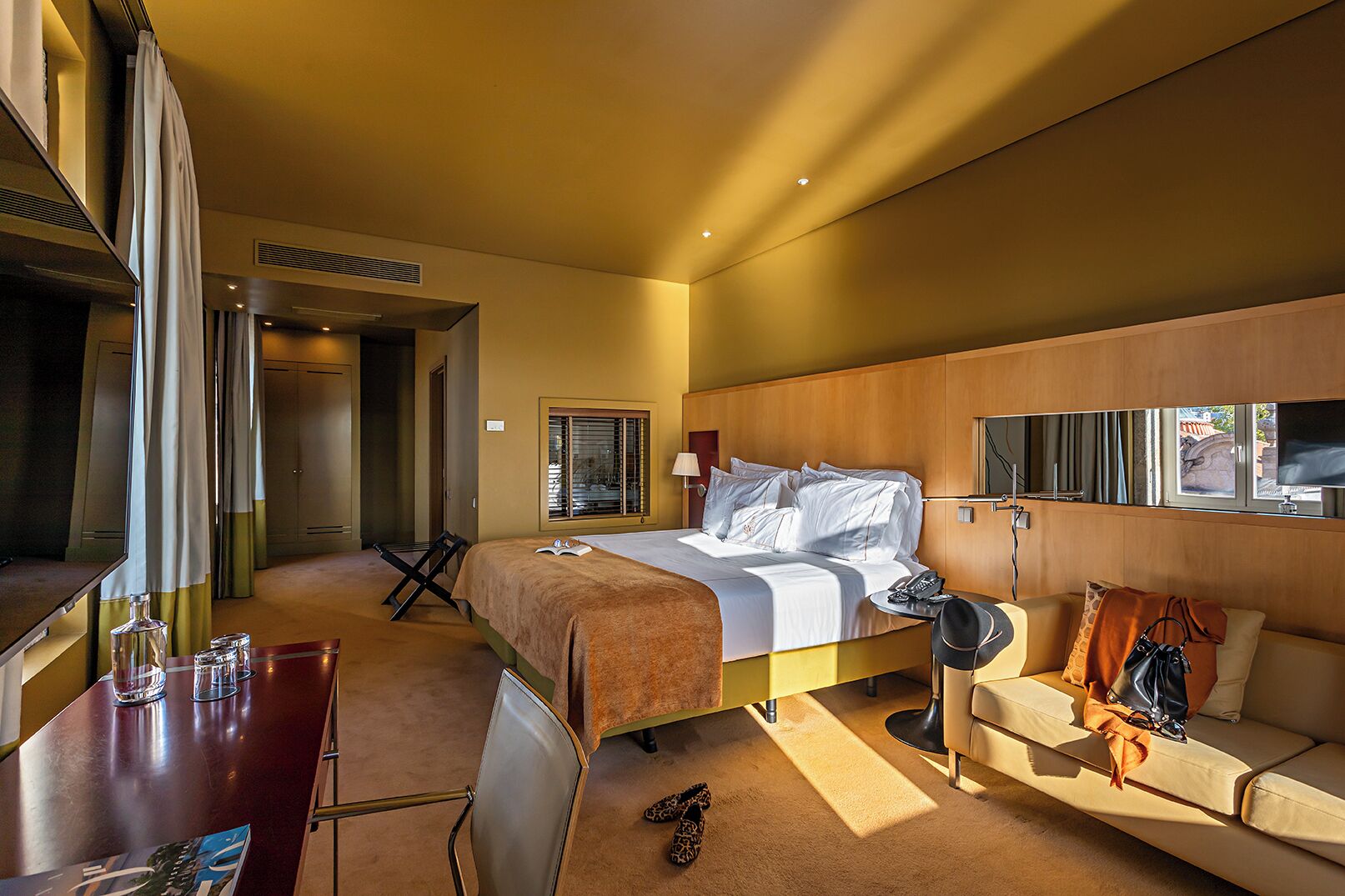 A hotel room with a bed, a desk, a chair, a sofa, and a TV.