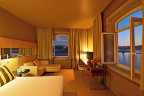 A hotel room with a bed, a desk, a chair, a sofa, a TV, and a view of a body of water.