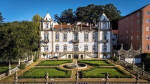 Un edificio imponente con fachada simétrica, una escalinata central y un jardín cuidado con una fuente.